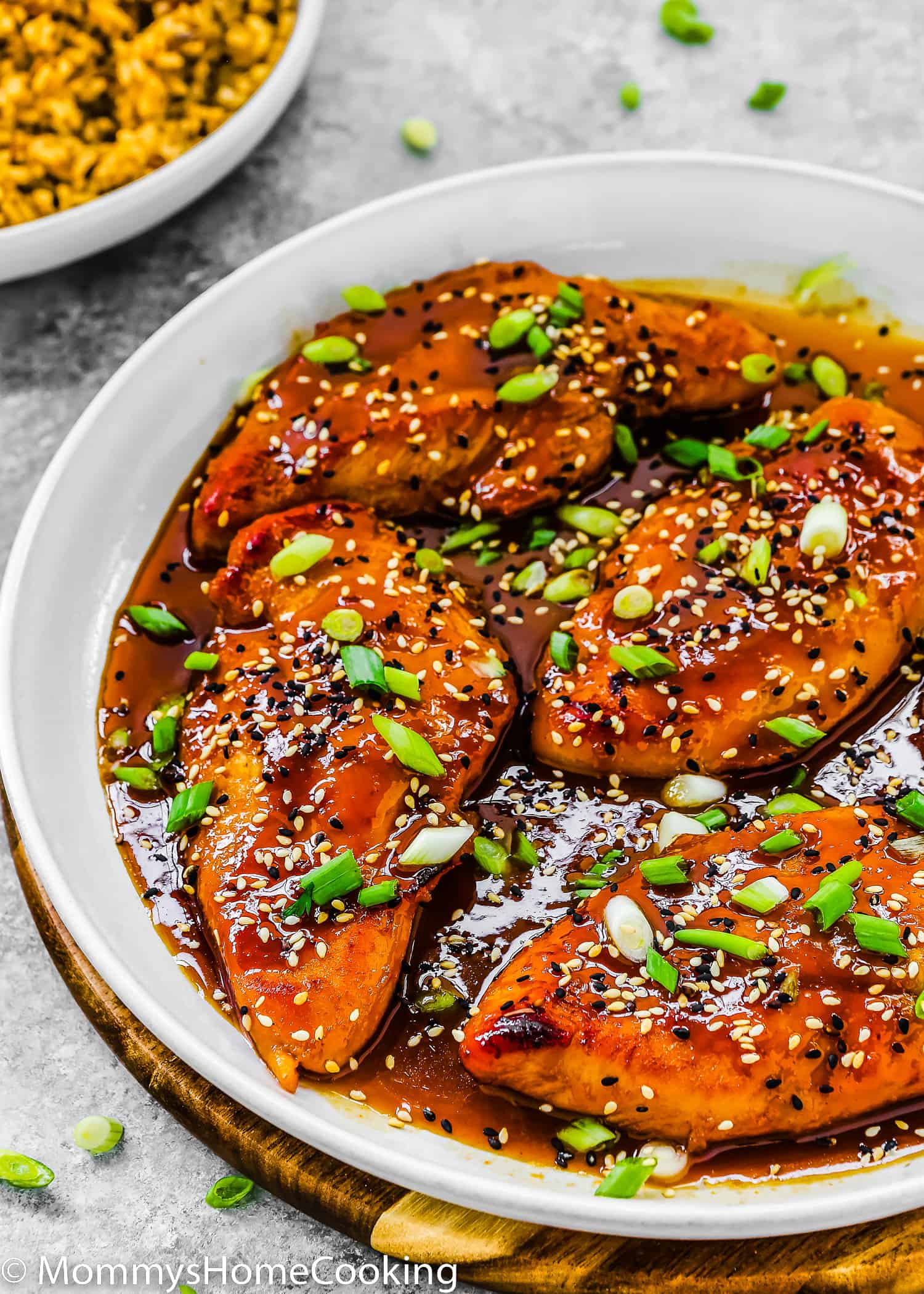 Asian-Style sticky Chicken Breasts in a white skillet garnished with green onion and sesame seeds.