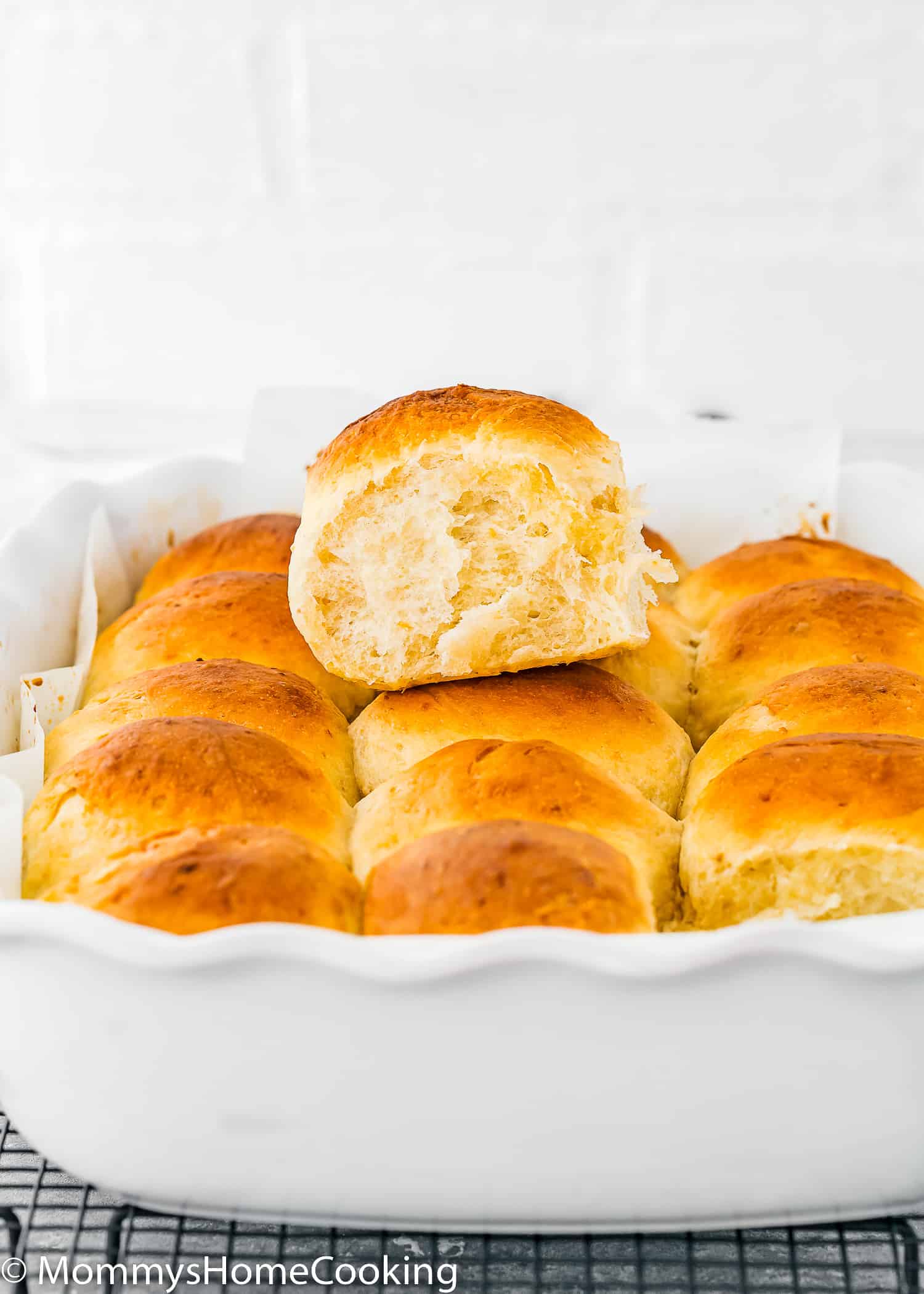 a egg-free homemade hawaiian roll over a baking pan with more rolls.