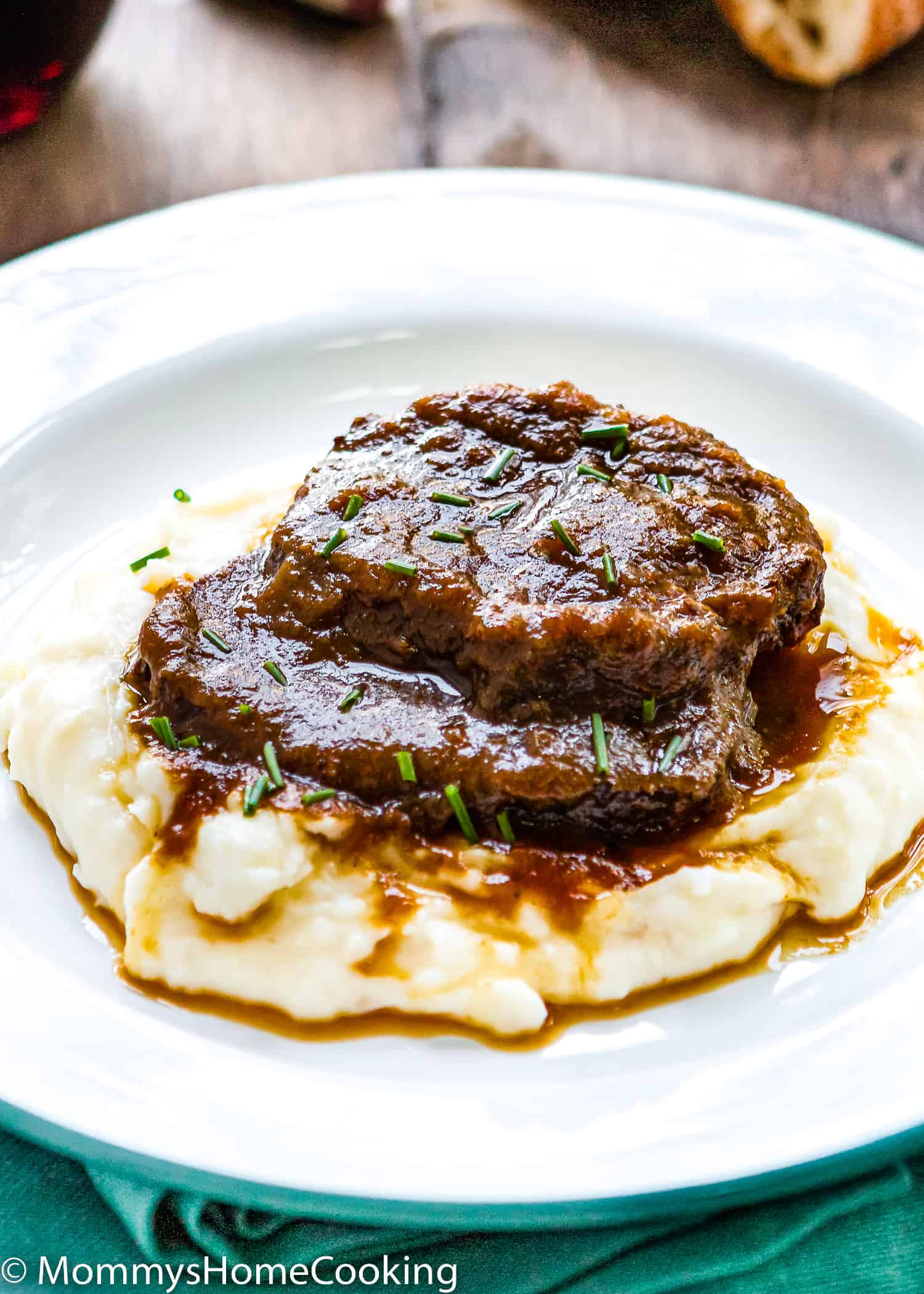 two slices of Venezuelan Asado Negro with sauce over mashed potatoes on white plate.