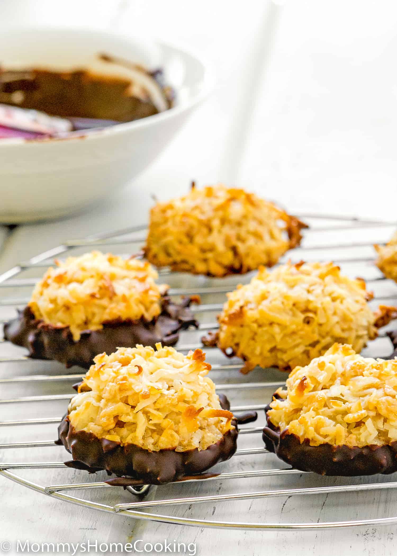 Eggless Coconut Macaroons dipped in chocolate over a cooling rack.