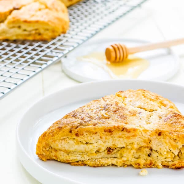 an eggless Bacon Cheddar Scone on a plate with a cooling rack with more scones on the background.