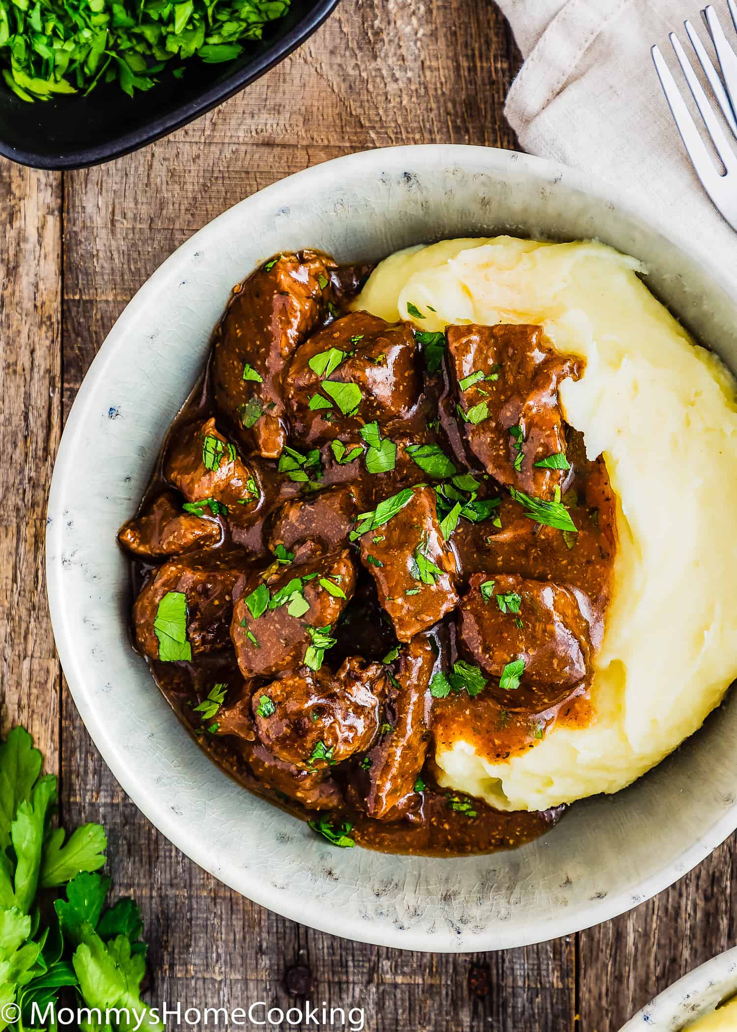 Easy Beef Tips with Gravy in a bowl with mashed potatoes and garnished with parsley.