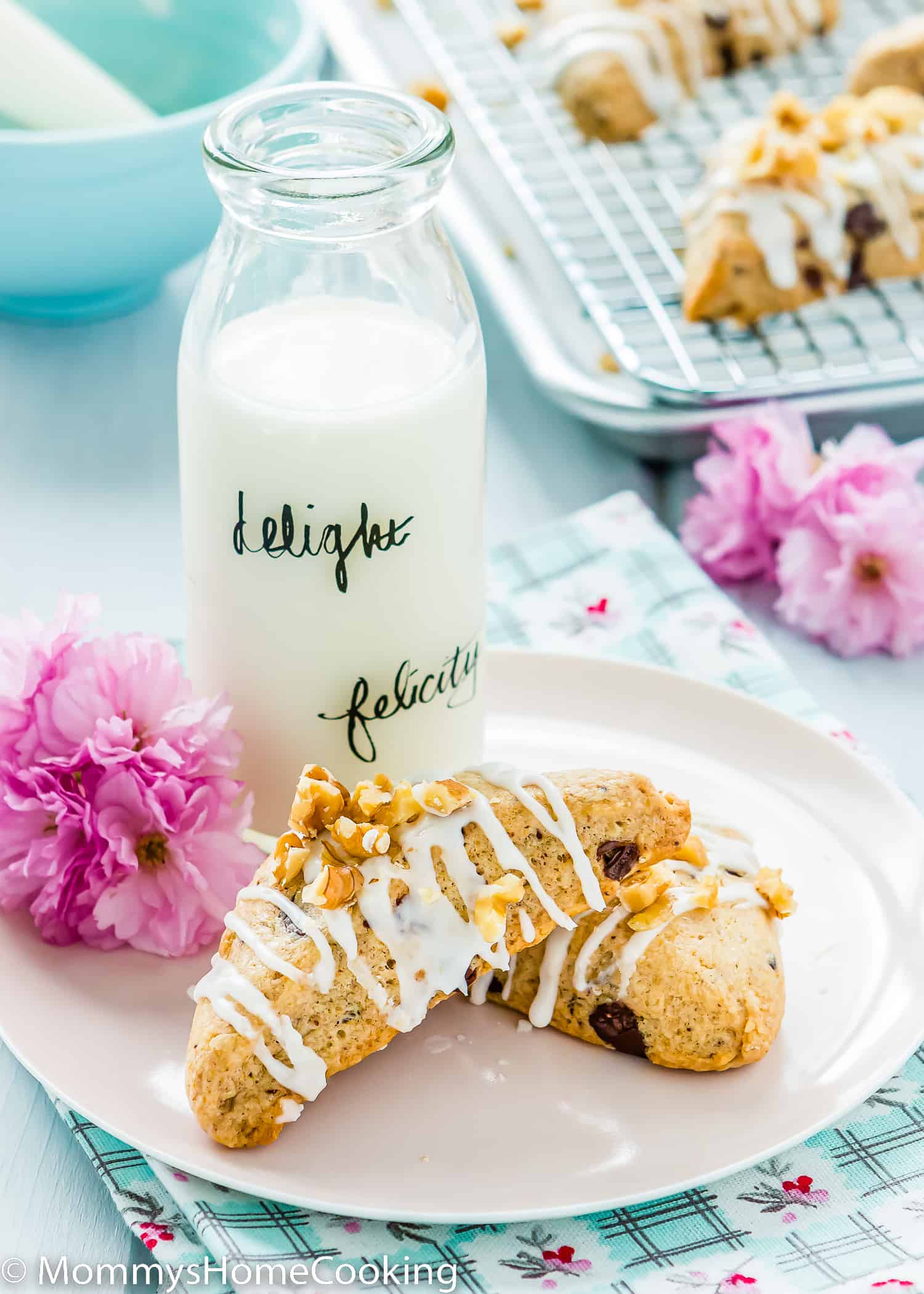 two Eggless Chocolate Chip Scones with glaze and chopped nuts over a pink plate and a bottle of milk on the side.