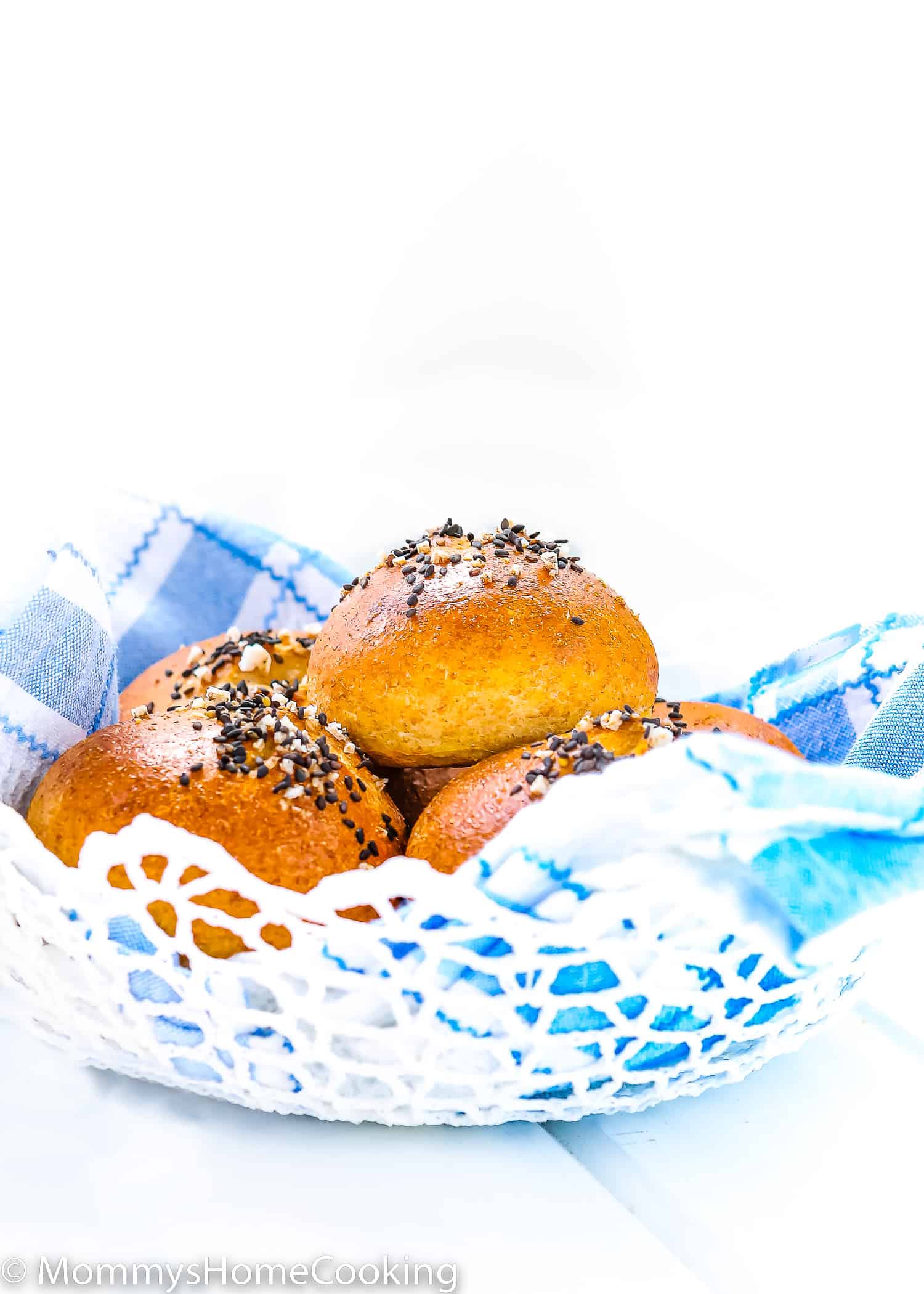 Eggless Honey Whole Wheat Rolls in a bread basket with a blue kitchen towel over a white surface.