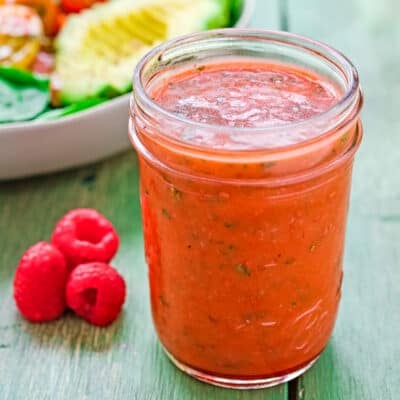 Raspberry Vinaigrette in a jar with fresh raspberries on the side and a salad in the background.