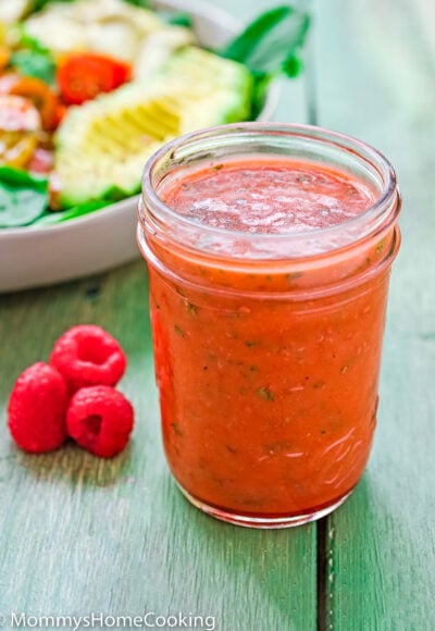 Raspberry Vinaigrette in a jar with fresh raspberries on the side and a salad in the background.