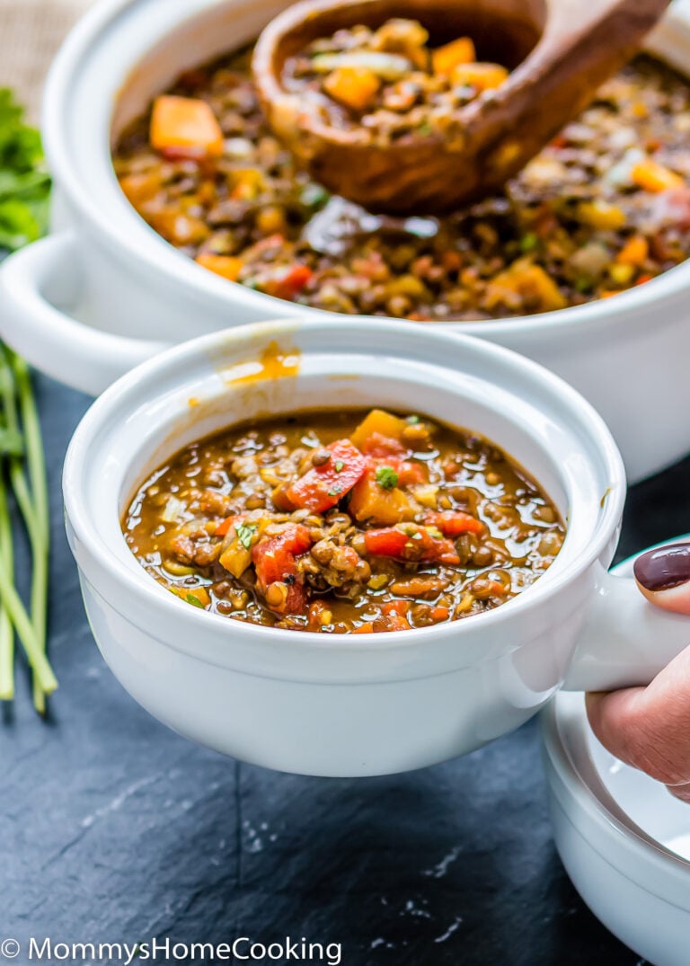 a hand holding a small bowl with Lentils and butternut Squash Soup.
