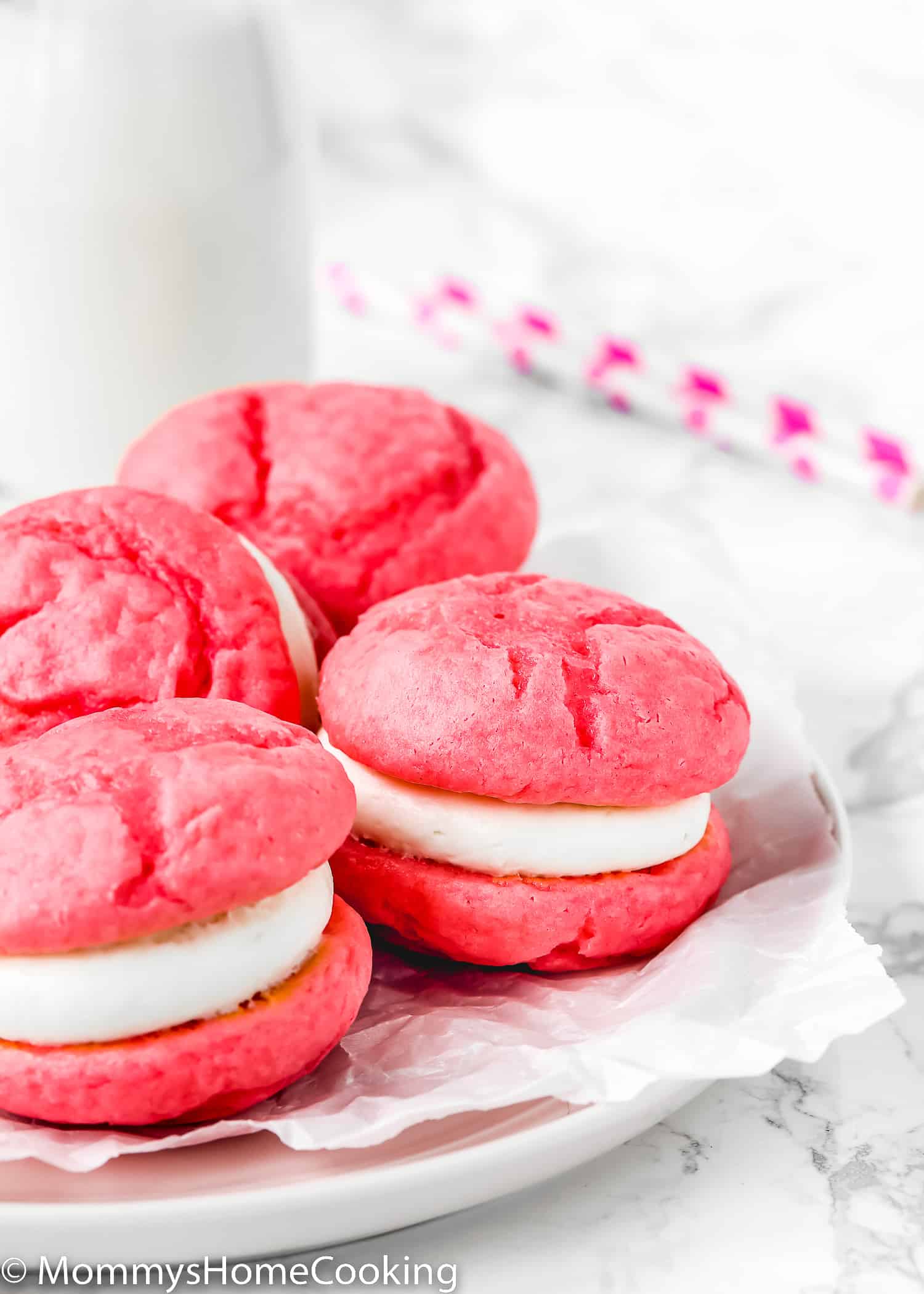Eggless whoopie pies on a plate with a glass of milk in the background.