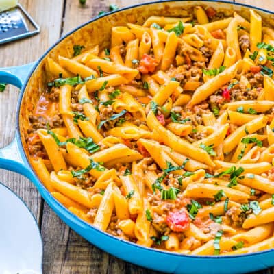Creamy Sausage Pasta in a skillet over a wooden surface with a serving spoon on the side.