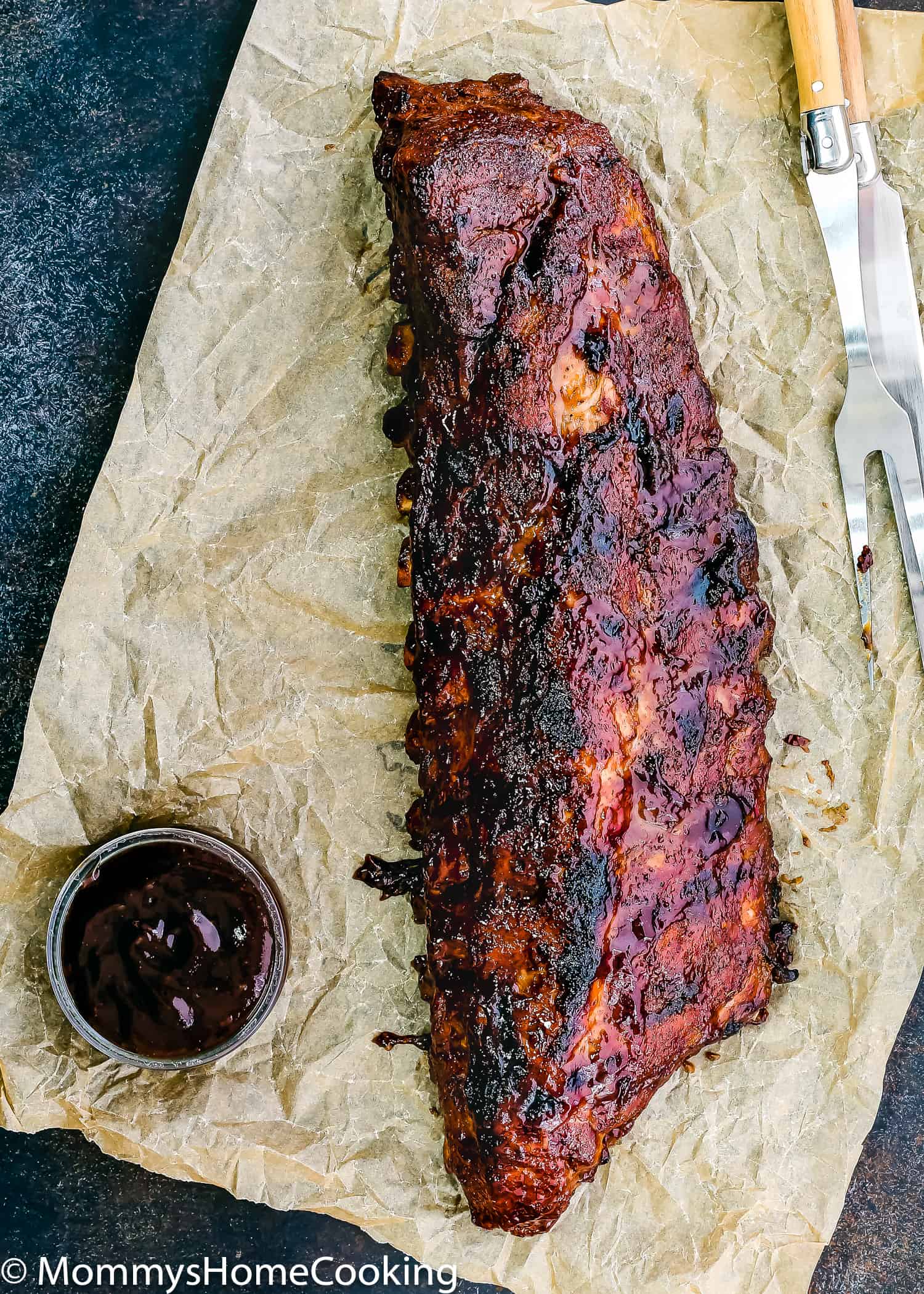 A rack of Fall-of-the-bone barbecue ribs over parchment paper and barbecue sauce on the sauce.
