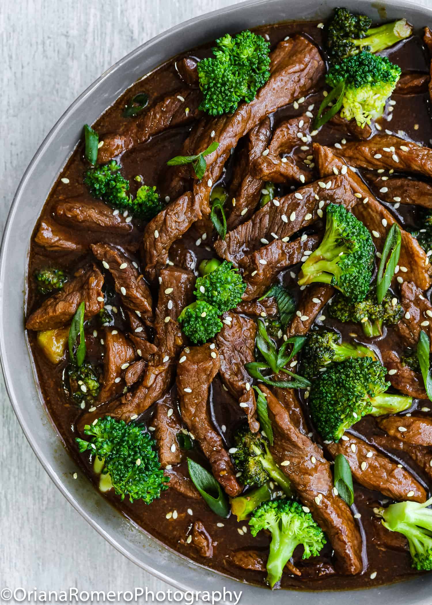 Beef and broccoli stir fry on a serving plate over a gray surface.