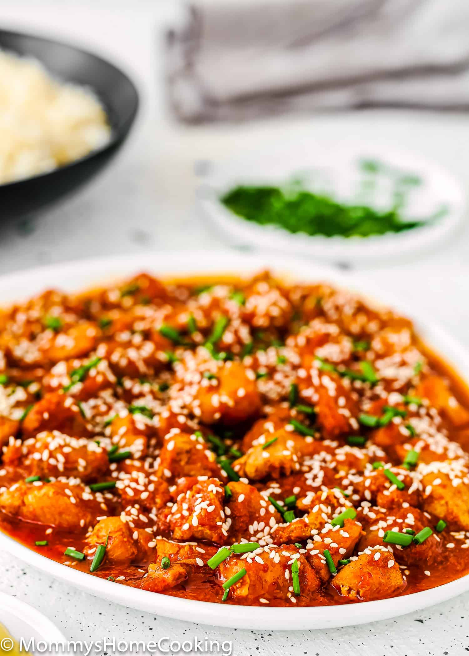 Korean Kimchi Chicken with sesame seeds and green onions on a plate.