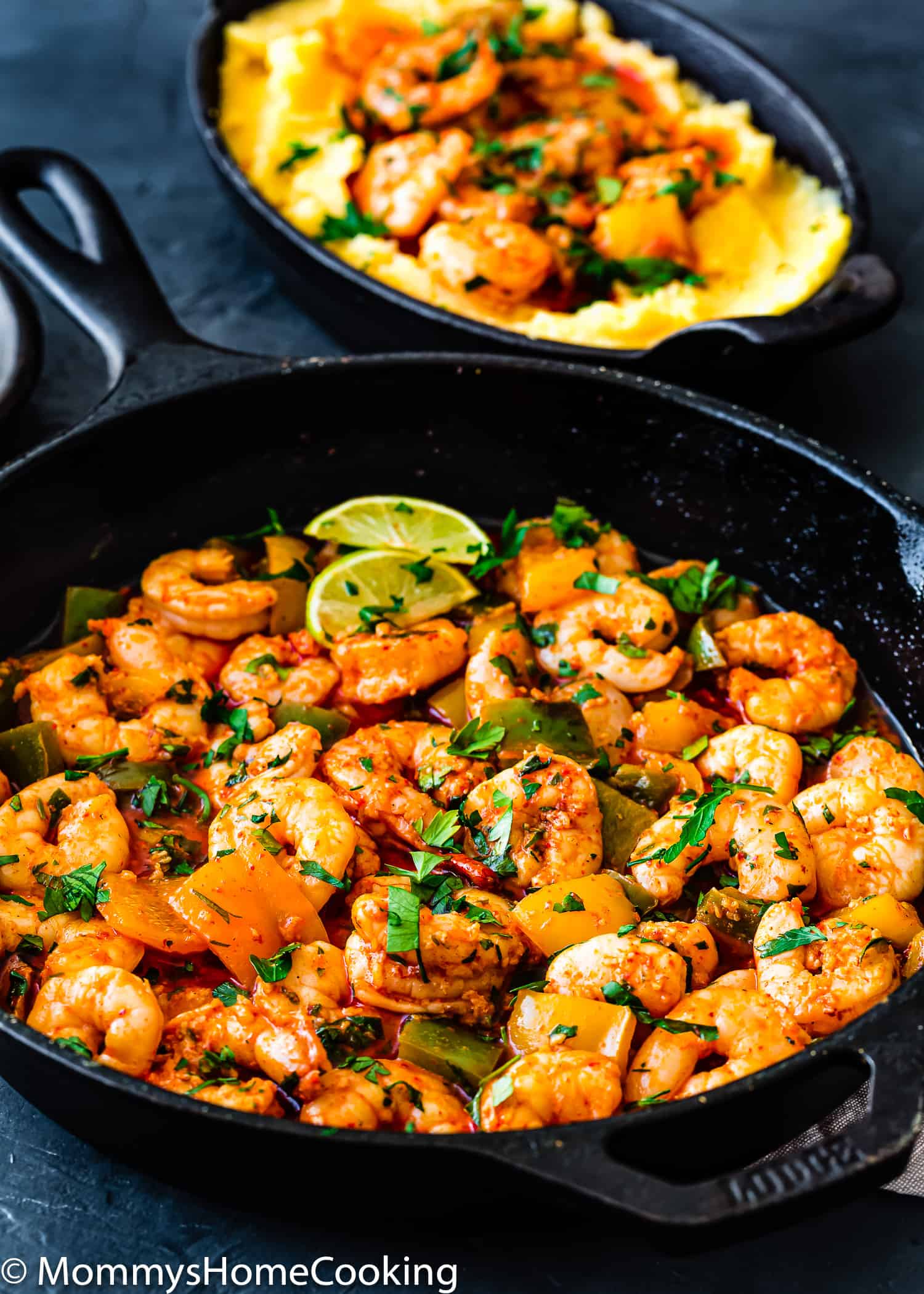 peri peri shrimp in a skillet with chopped parsley and lime wedges. 
