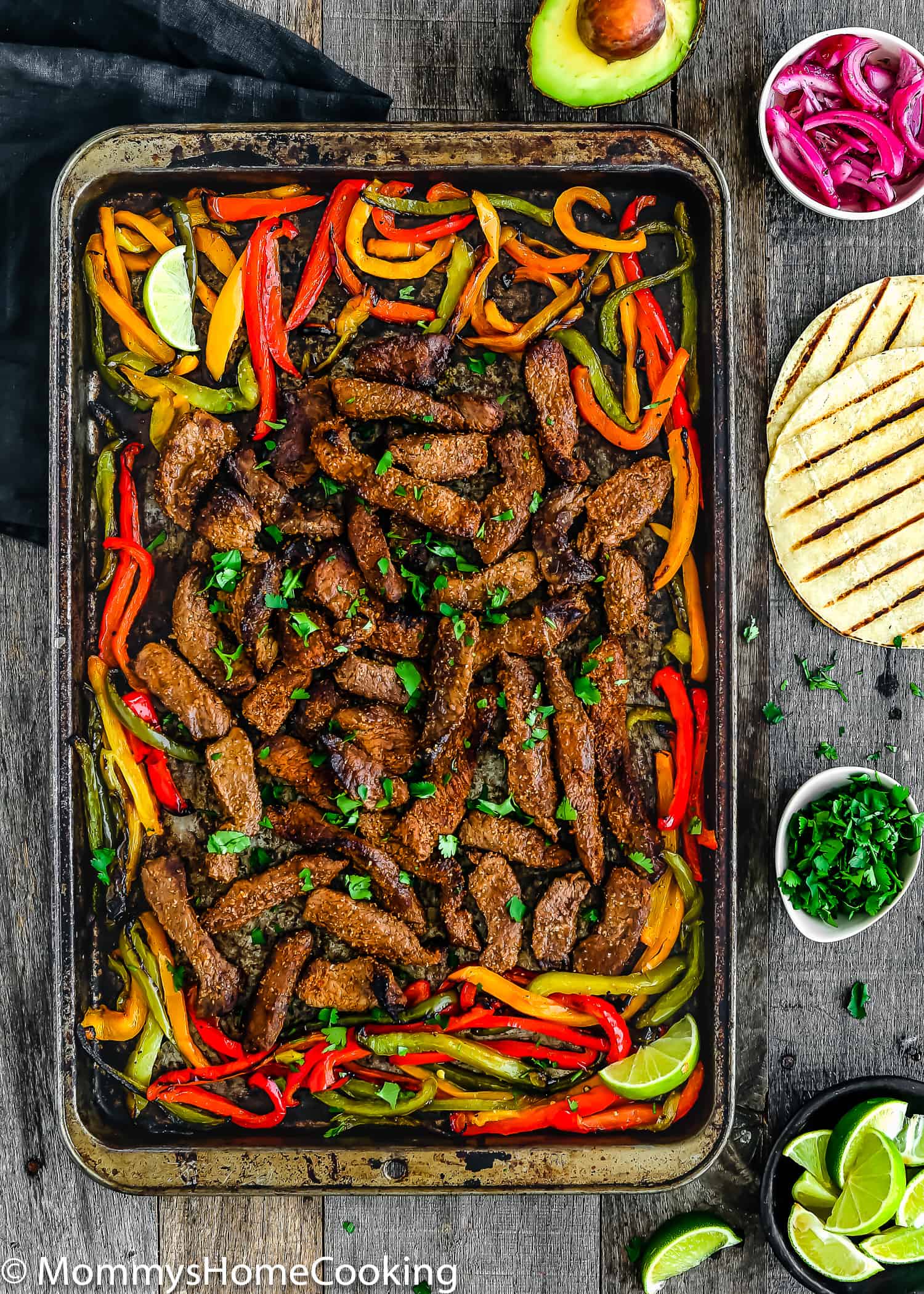 Easy Sheet Pan Steak Fajitas on a baking sheet with toppings on the side.