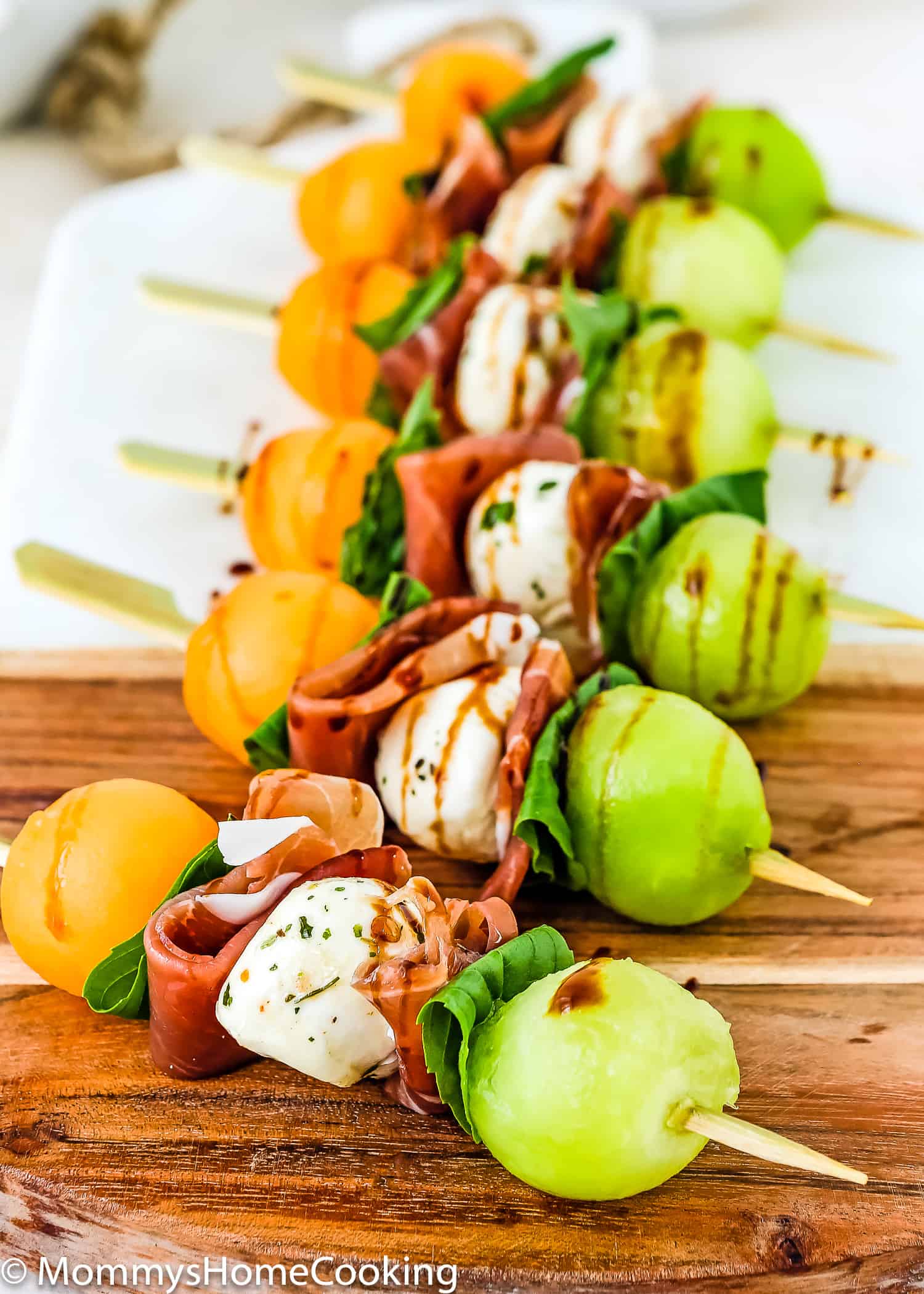 Prosciutto Melon appetizers on a cutting board drizzled with balsamic glaze.