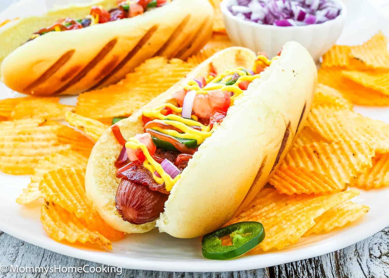 bacon wrapped hot dogs on a plate with potato chips.