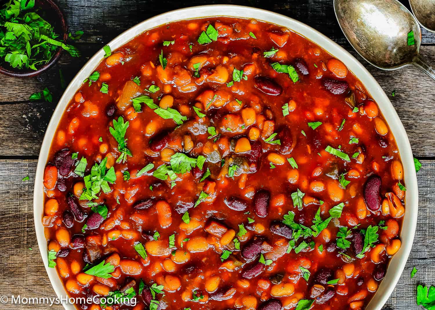 Homemade baked beans in a a bowl over a wooden surface.