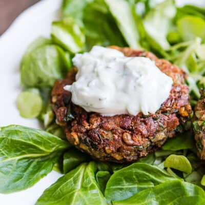 Healthy Easy Lentil Pattie with yogurt sauce on top over greens on a plate.