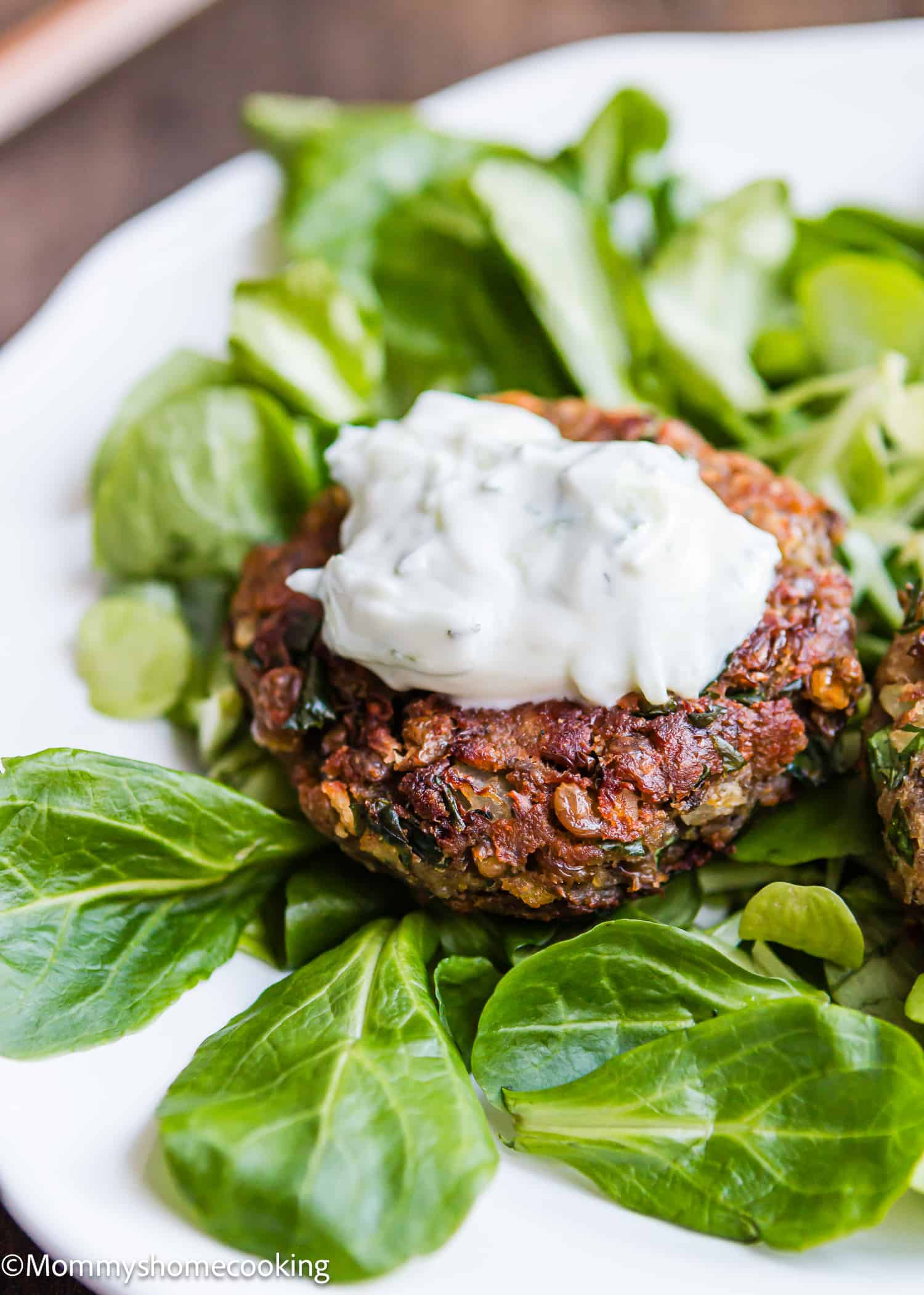 Healthy Easy Lentil Pattie with yogurt sauce on top over greens on a plate.