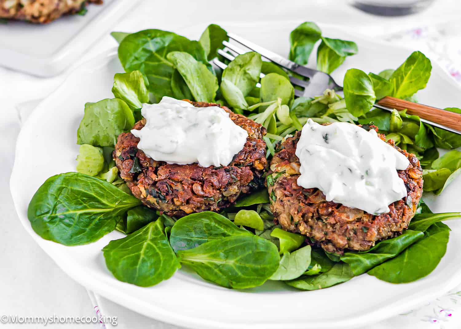 two Healthy Easy Lentil Patties with yogurt sauce on top over greens on a plate.