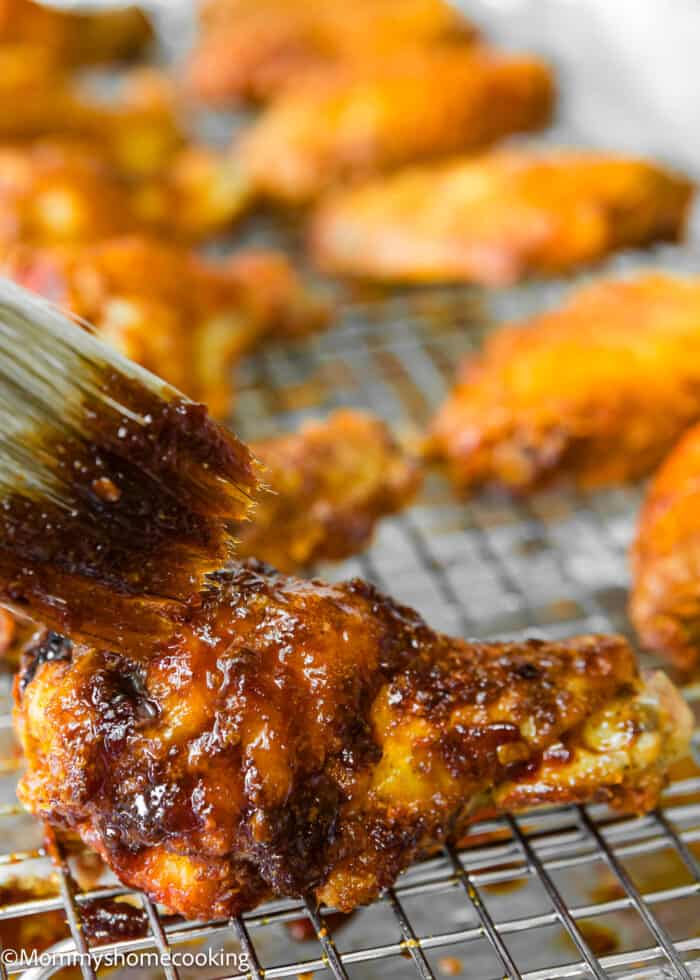 a kitchen brush glazing Baked Chicken Wings with chipotle sauce.