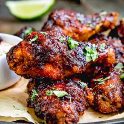 Chipotle Chicken Wings on a plate with chipotle sauce and a lime wedges on the side garnished with chopped cilantro.