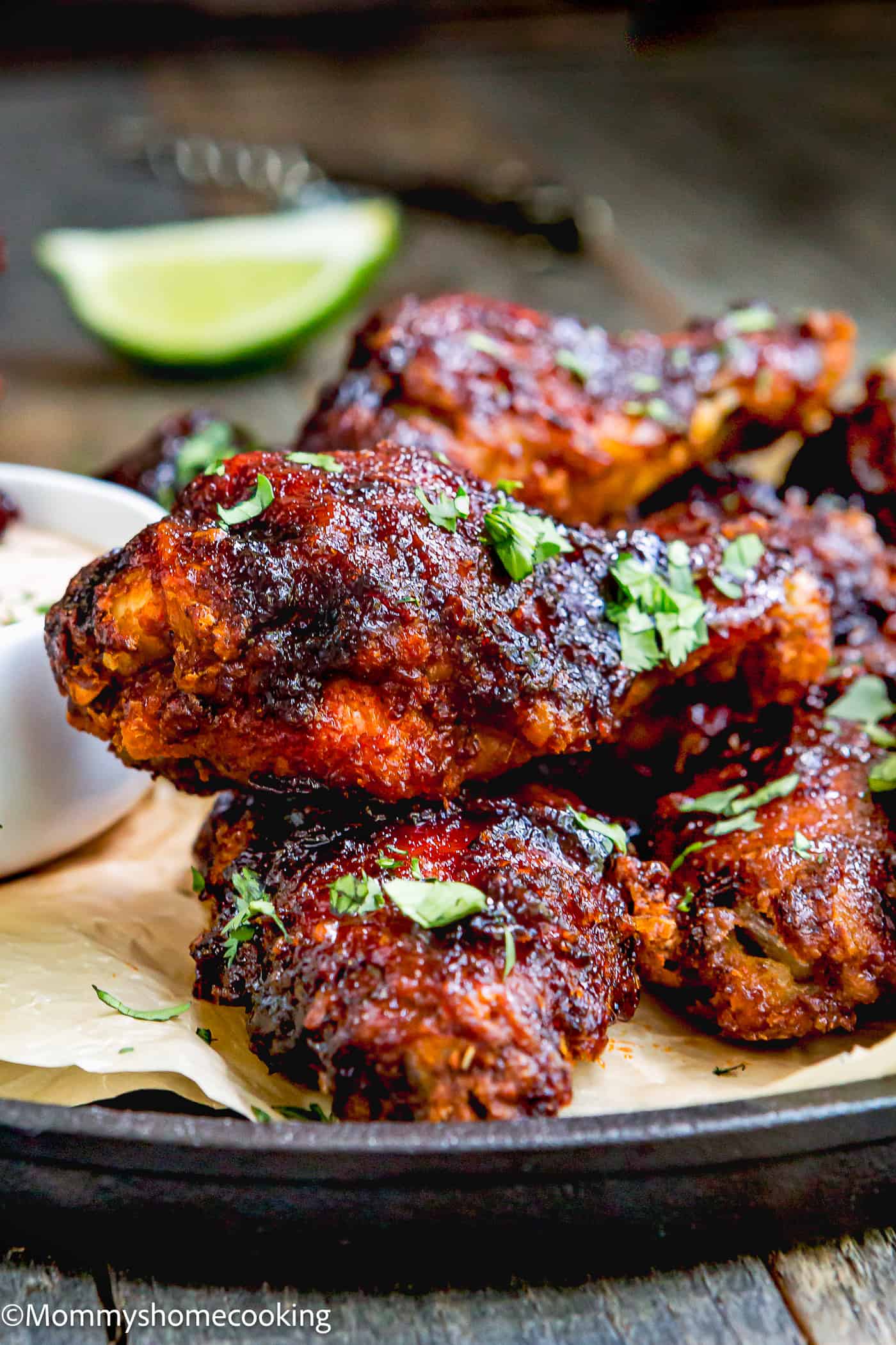 Chipotle Chicken Wings on a plate with chipotle sauce and a lime wedges on the side garnished with chopped cilantro.