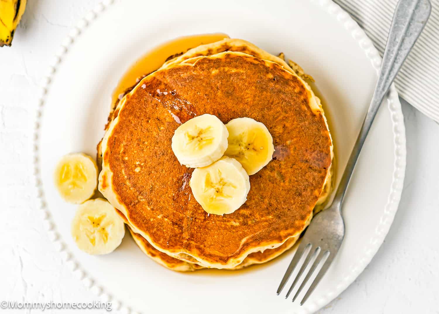 Overhead view of a a stack of easy banana pancakes made with no egg on a white plate with a fork.