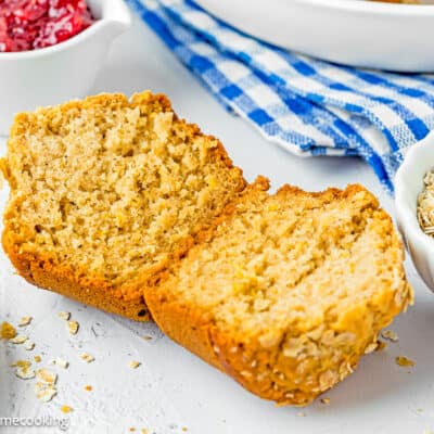 A healthy oat muffin cut in half is sitting on a table next to a bowl of oats.