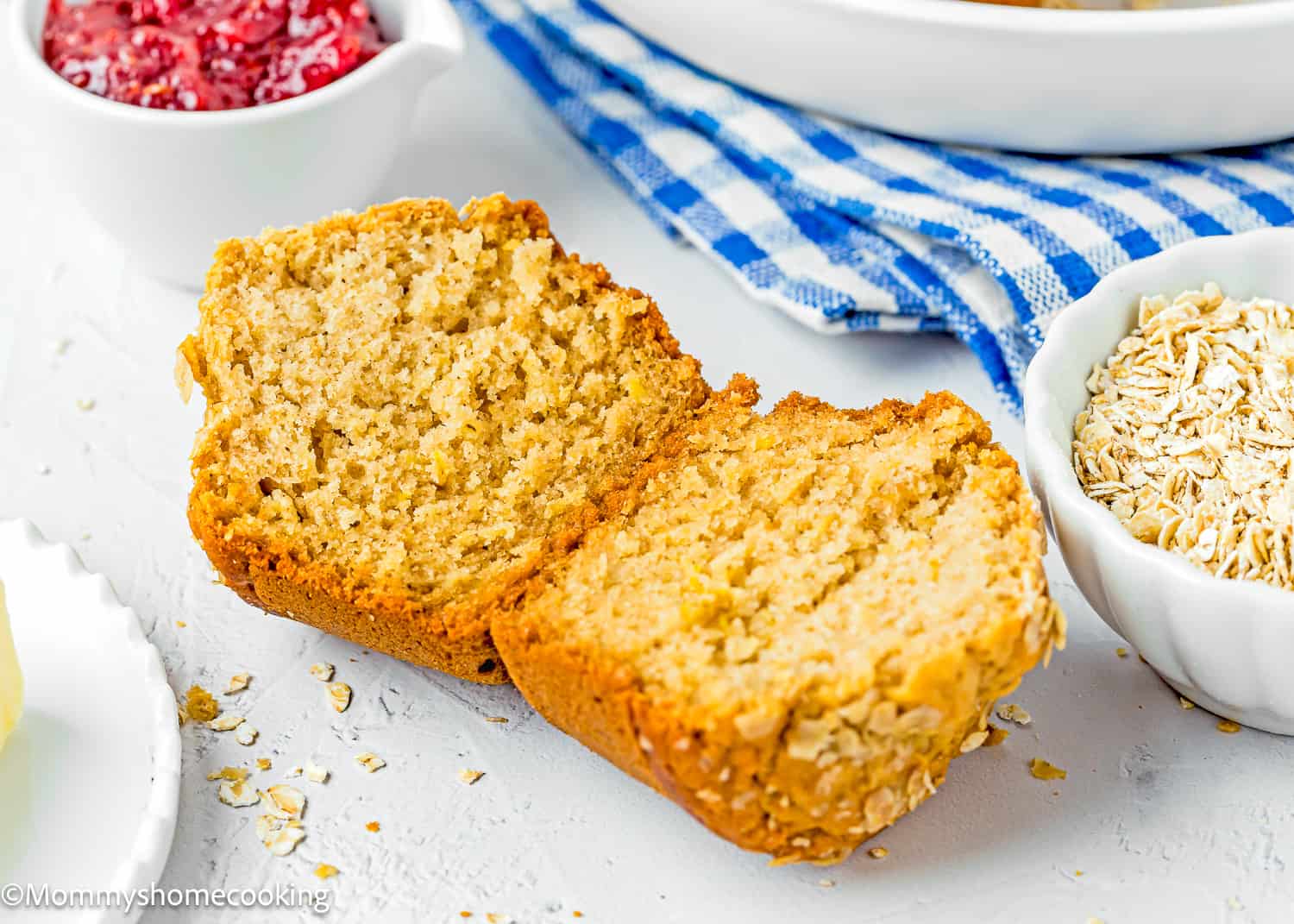 A healthy oat muffin cut in half is sitting on a table next to a bowl of oats.