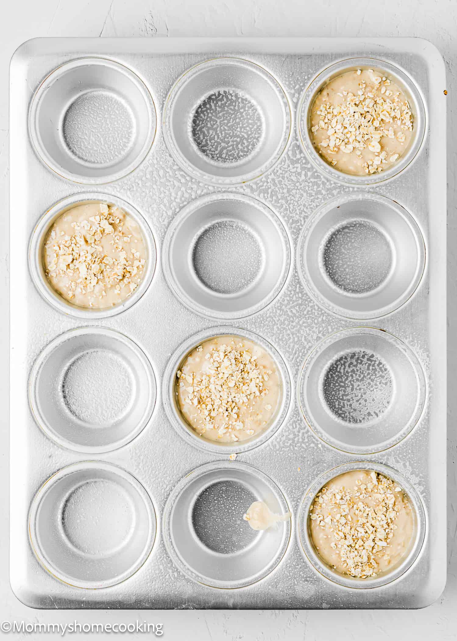 A muffin tin filled with easy oat muffins batter topped with more oats, made without eggs, dairy, or sugar.