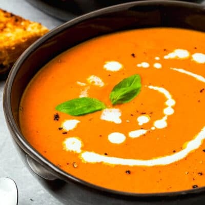 a bowl with homemade Tomato Soup drizzled with cream, basil leaves, and black pepper