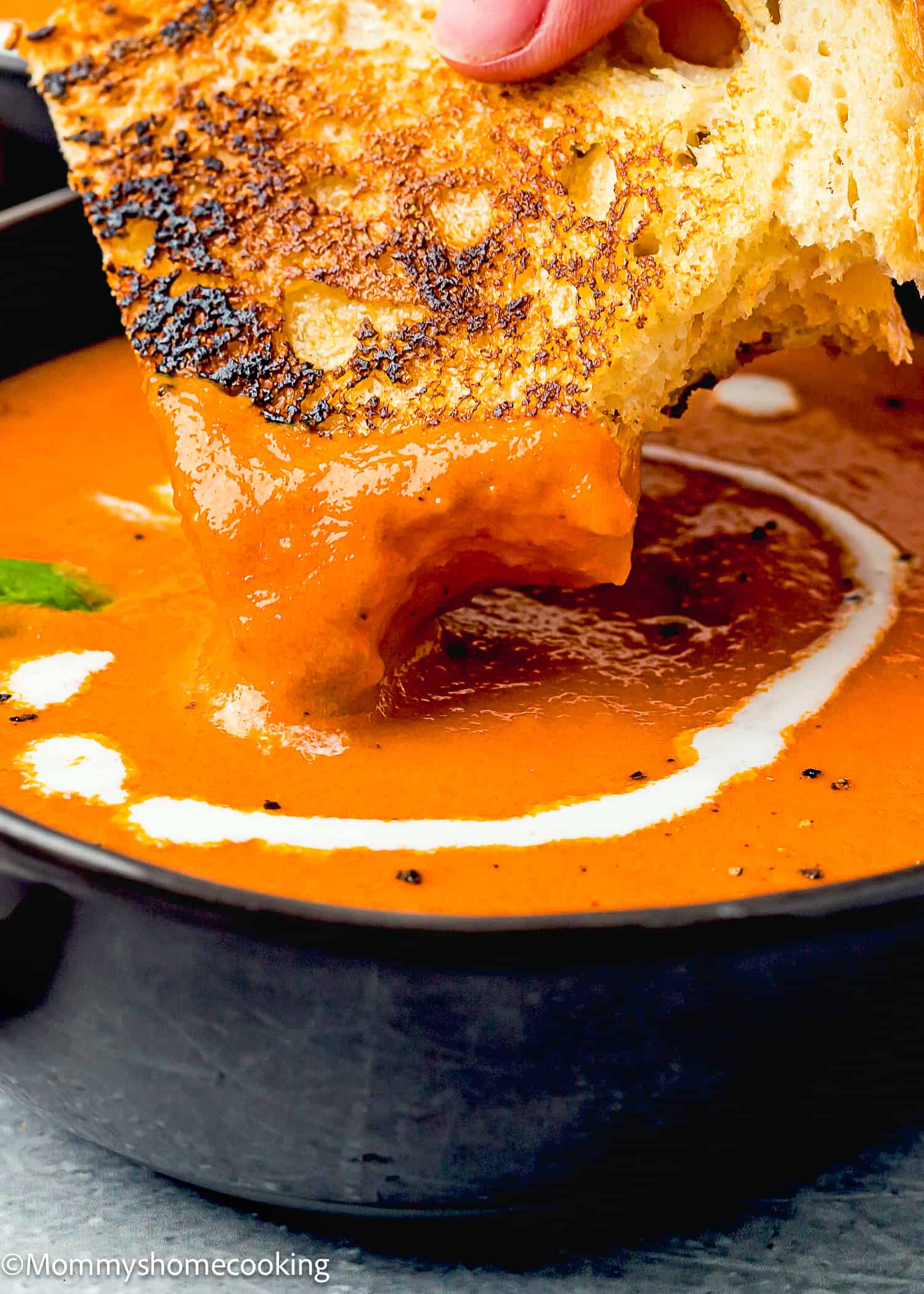 a woman hand holding a grilled cheese sandwich and dip it into a bowl with homemade tomato soup.