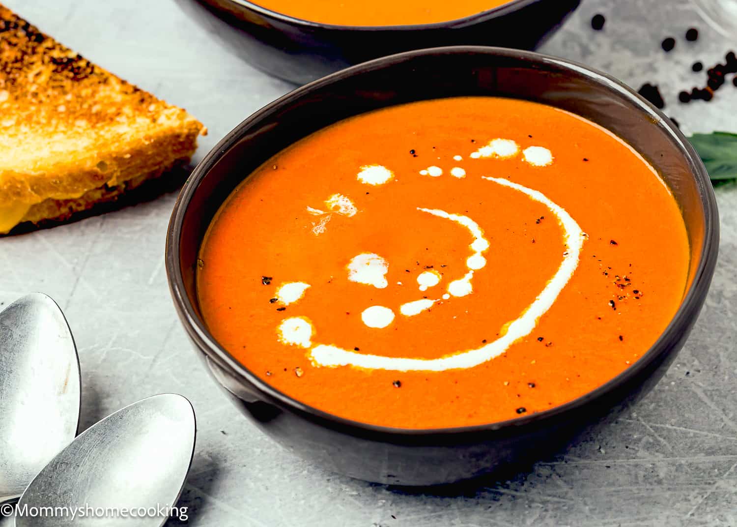 a bowl with homemade Tomato Soup drizzled with cream a black pepper.
