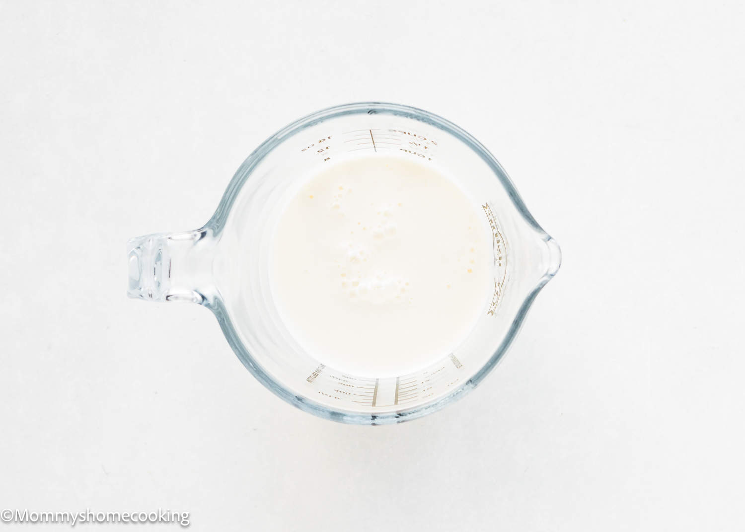 A glass measuring cup filled with creamy milk.