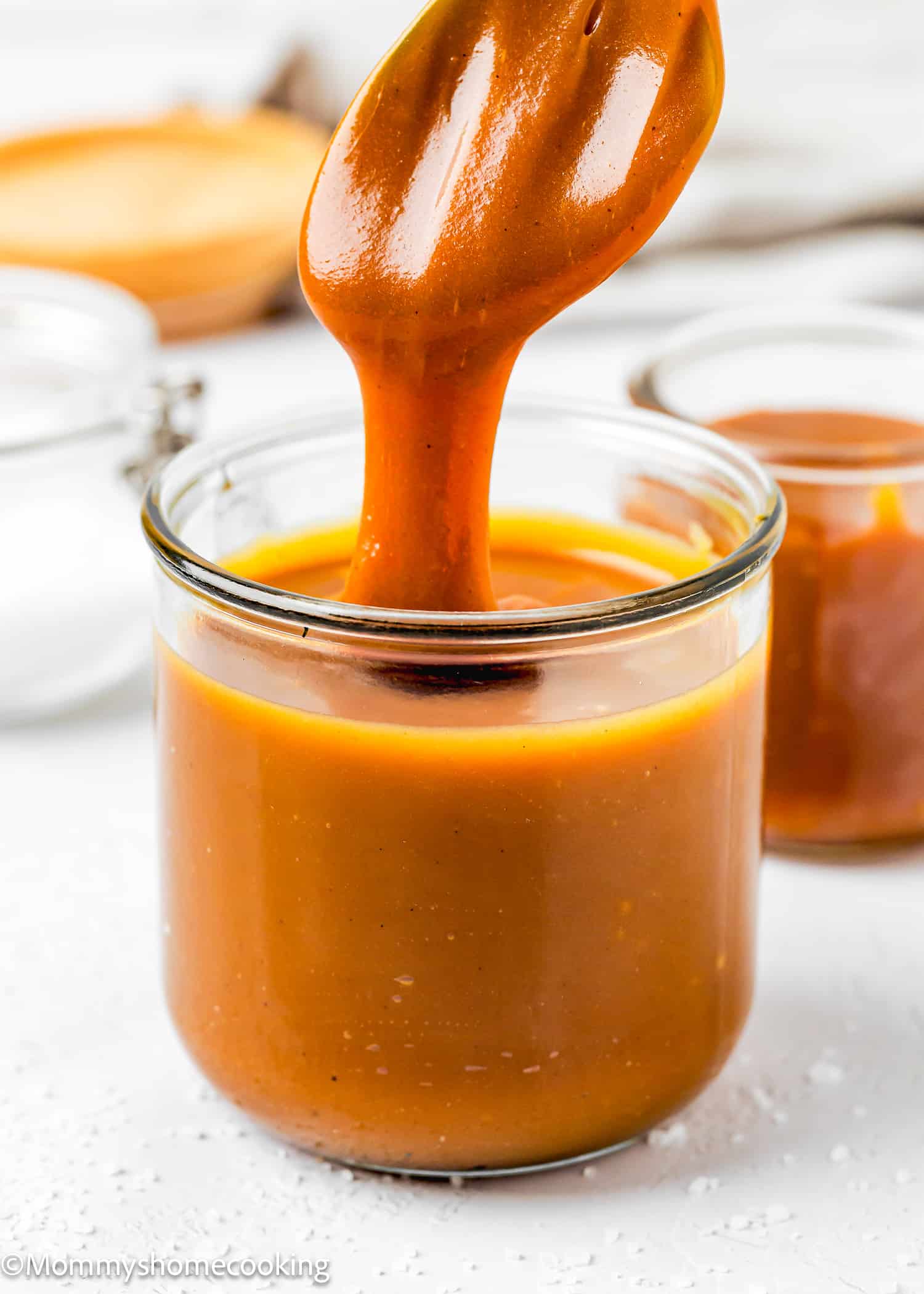 A spoon dipped into a jar of salted caramel sauce.