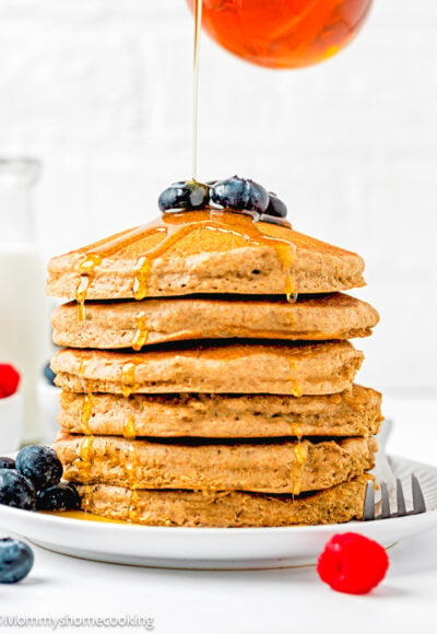 Whole Wheat Pancakes stack with fresh blueberries on top on a plate with maple syrup being poured.