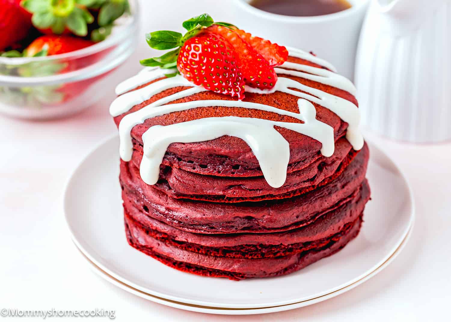 five egg-free red velvet pancakes with cream cheese topping and a strawberry on a plate.