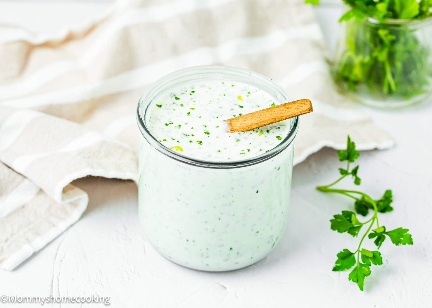 Venezuelan Garlic Sauce (Salsa de Ajo Venezolana) in a glass container with a wooden and a kitchen towel in the background.