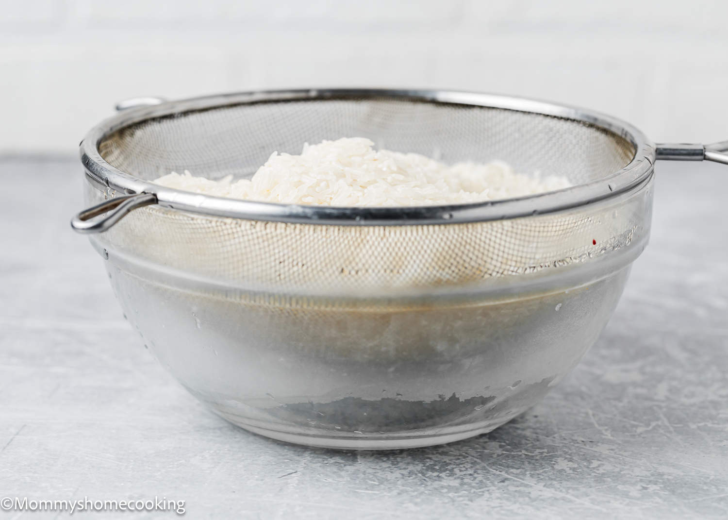 rinsed rice in a colander over a glass bowl.