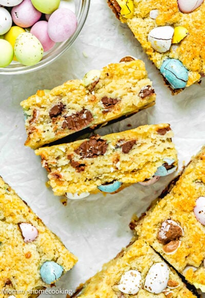 Easter Blondie cut in half showing its inside texture over a white surface with more blondies and chocolate around it.