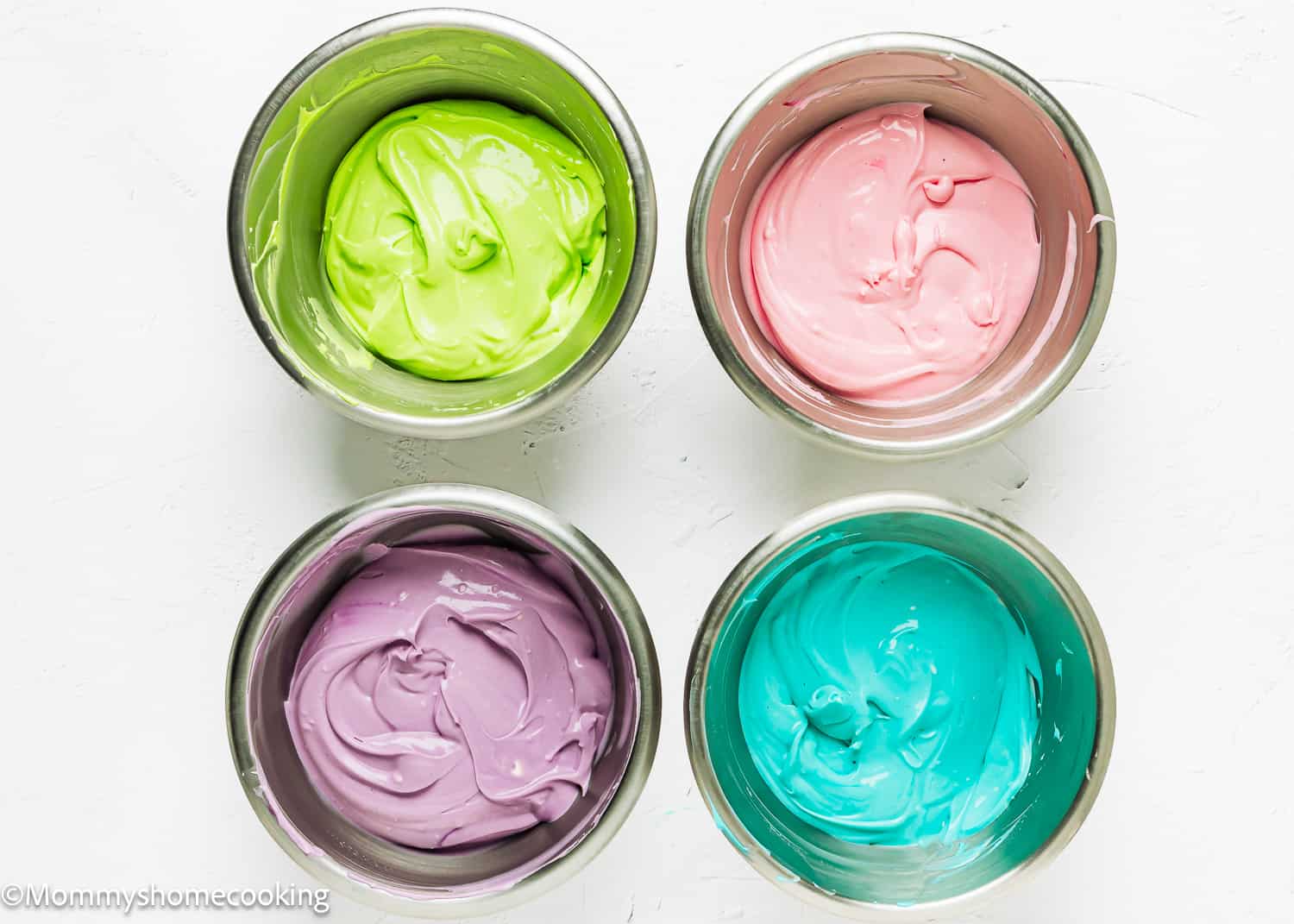 four metals bowls with egg-free cheesecake batter colored with four different colors.
