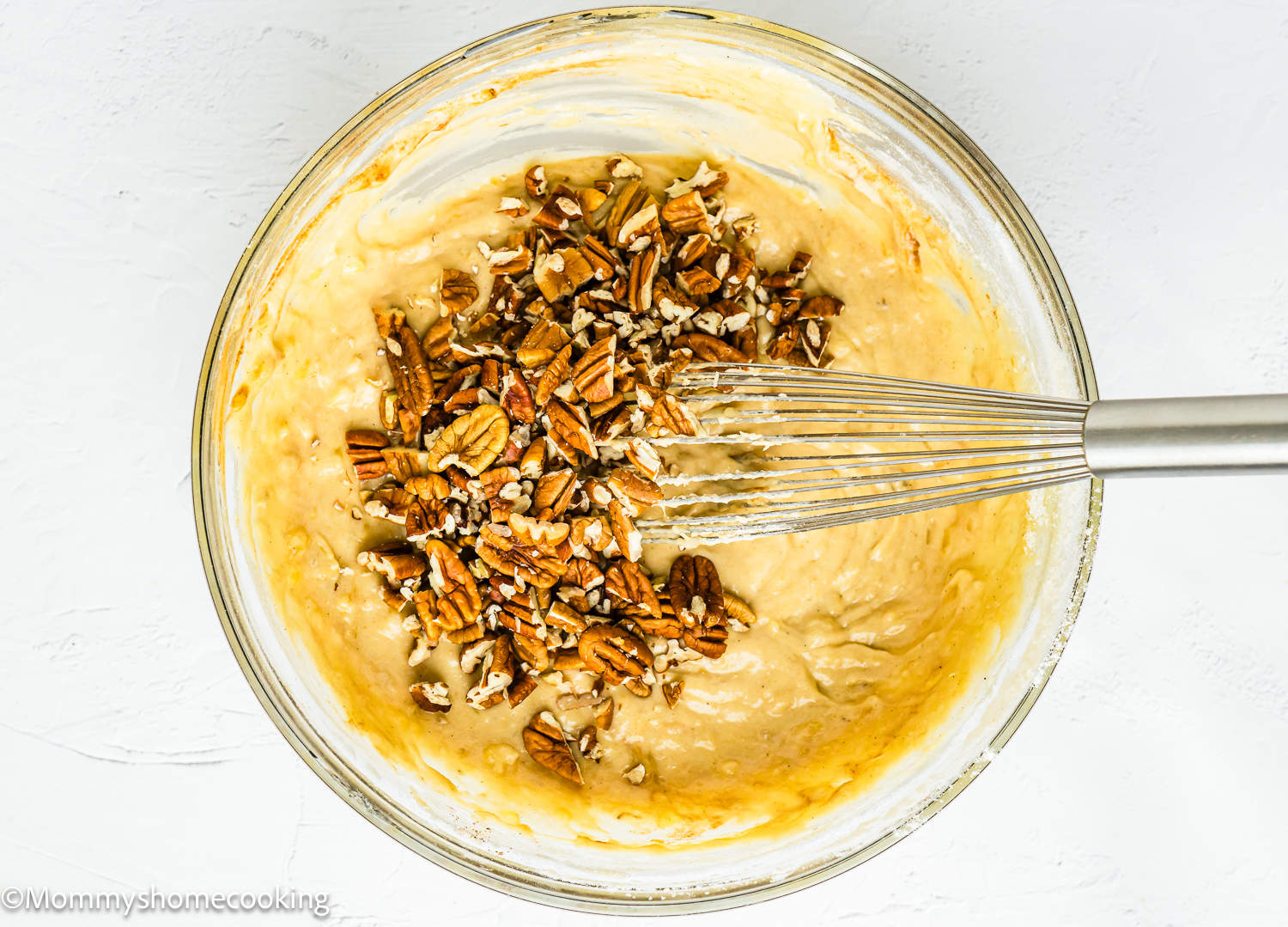 Easy Banana Nut Bread Without Eggs batter with chopped pecans and a whisk in a bowl.