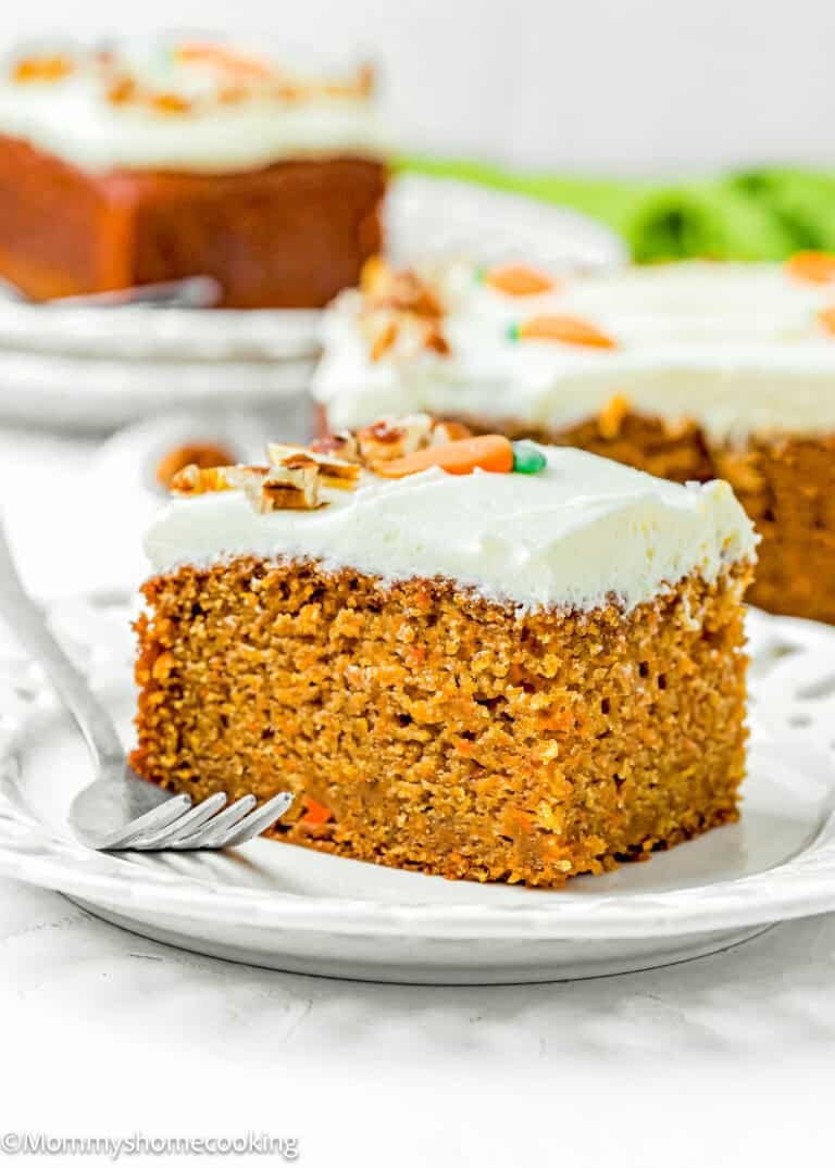 A slice of Easy Carrot Cake Snack Cake (No Eggs – No Dairy) with cream cheese frosting and chopped nuts on a white plate with a fork.