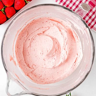 easy homemade strawberry frosting in a stand mixer bowl over a white surface with fresh strawberries in the side and a red kitchen towel.