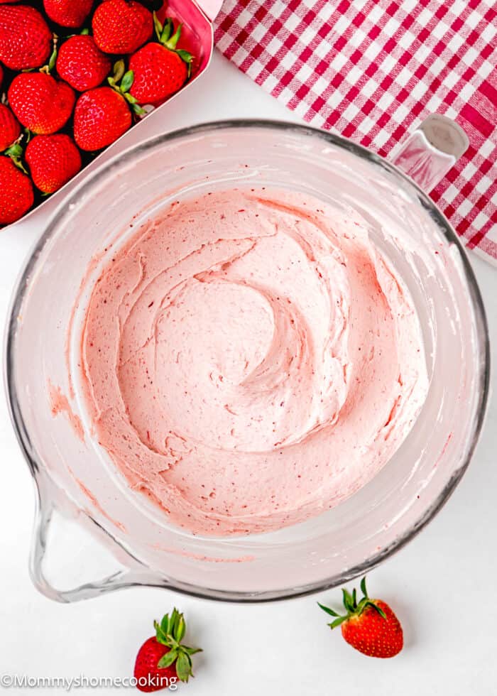 easy homemade strawberry frosting in a stand mixer bowl over a white surface with fresh strawberries in the side and a red kitchen towel.