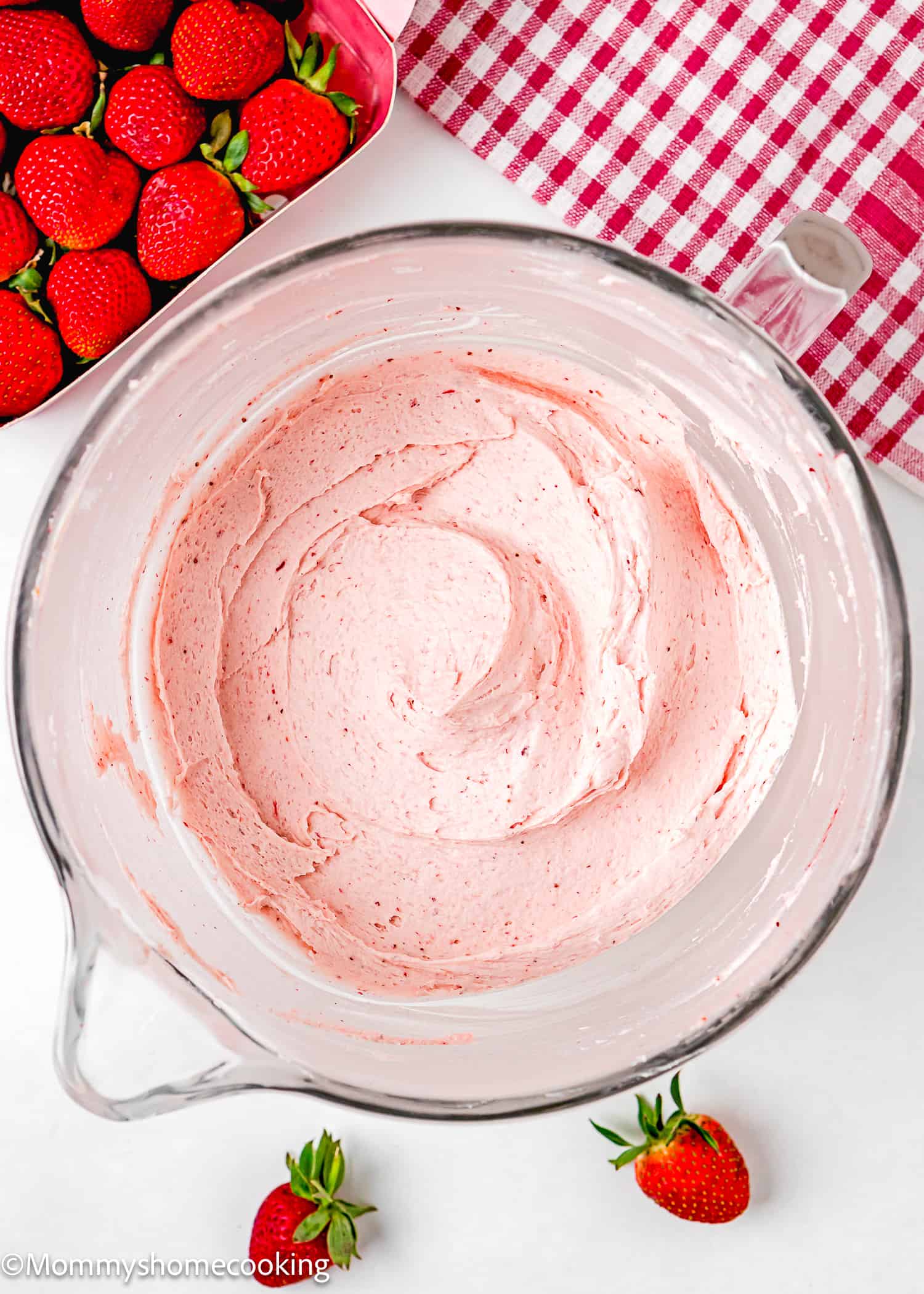 easy homemade strawberry frosting in a stand mixer bowl over a white surface with fresh strawberries in the side and a red kitchen towel.