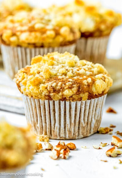 Hummingbird Muffins with crumb on top on a white surface with more muffins in the background.