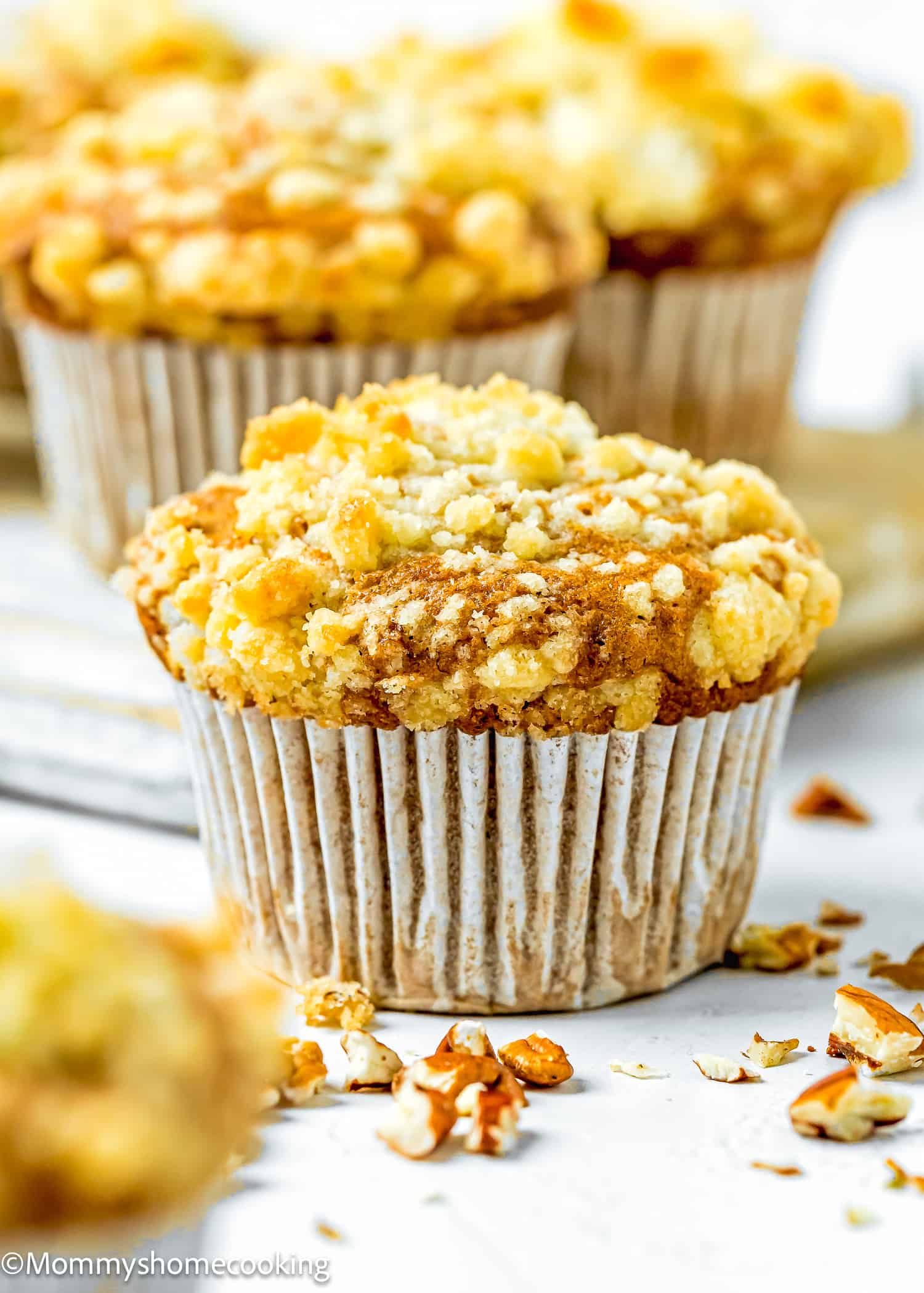 Hummingbird Muffins with crumb on top on a white surface with more muffins in the background.