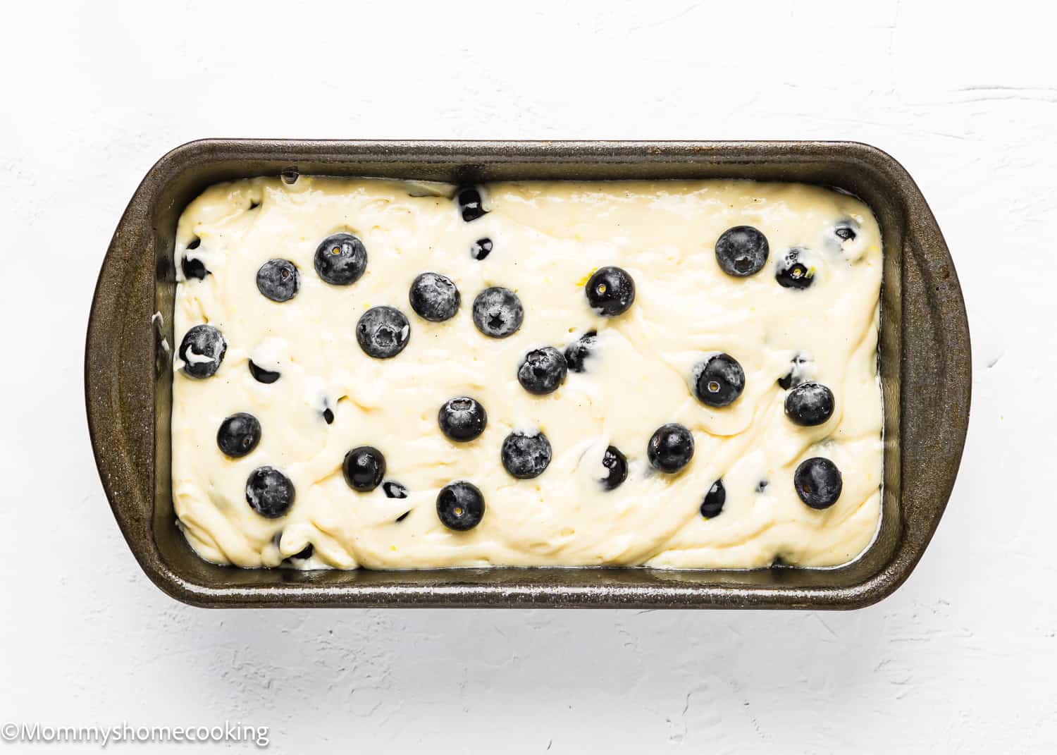 Eggless Lemon blueberry Loaf Cake batter in a loaf pan with more blueberry on top.